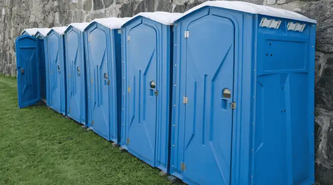 Row of blue portable toilets lined up on grass against a stone wall for event sanitation in Las Vegas, NV