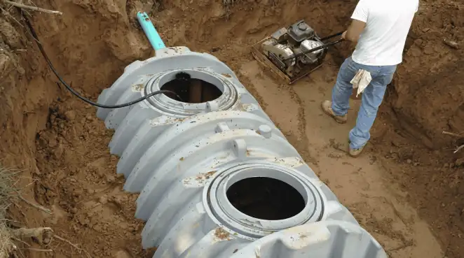 Septic tank installation showing a technician compacting soil around a new poly septic tank in an excavation pit in Las Vegas, NV